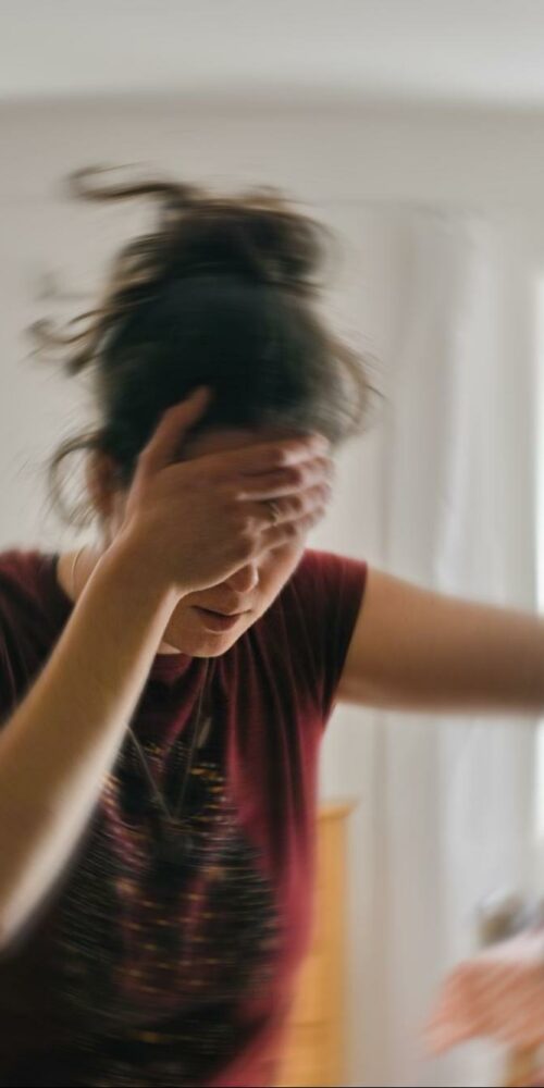 Person experiencing dizziness, holding their head and leaning on a door for support.