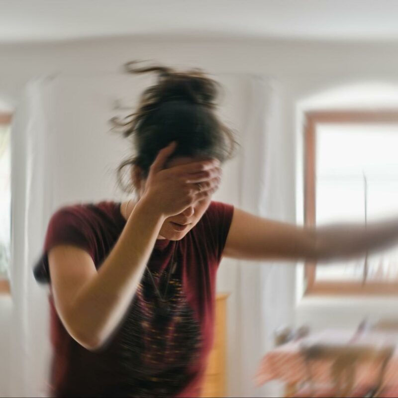 Person experiencing dizziness, holding their head and leaning on a door for support.